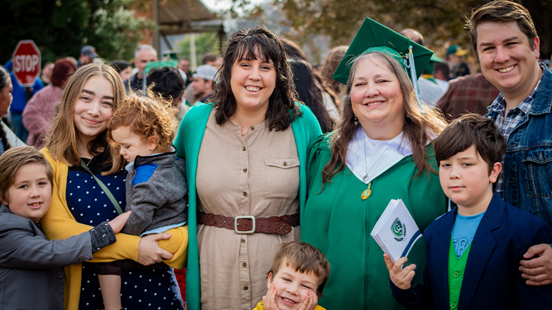 A family of eight people posing for a photo outside of a graduation ceremony.
