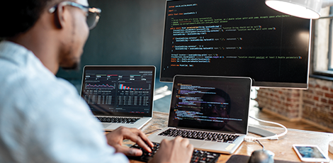 A man writing code on three different computers