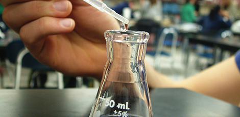 Someone adding liquid to a beaker using a pipette