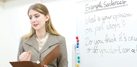 A woman standing in front of a whiteboard with english subjects written on it