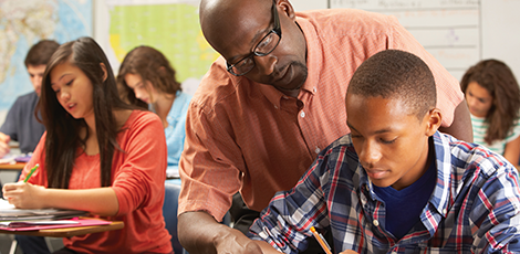 A teacher helping a student while the other students continue to work on their worksheet