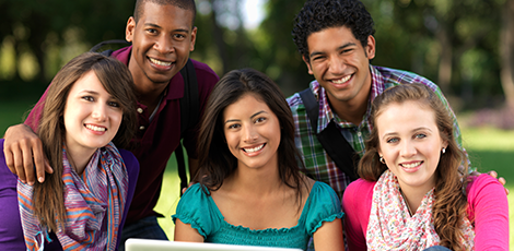 A group of people smiling ath the camera while using a laptop