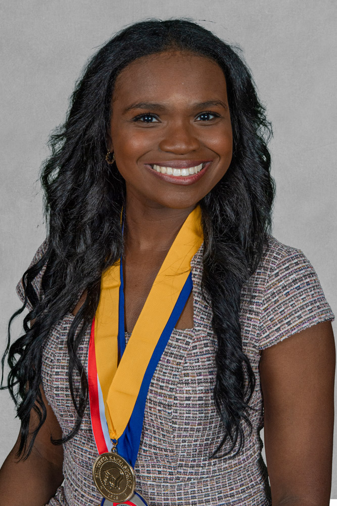 A dark-haired woman smiles for a photos while wearing two medals.