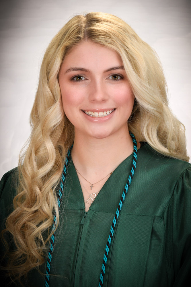 A blonde woman wearing a green graduation gown smiles for a photo.