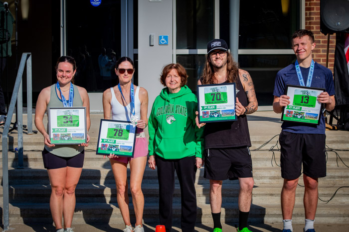 Five people pose for a photo holding framed pictures in front of concrete steps.