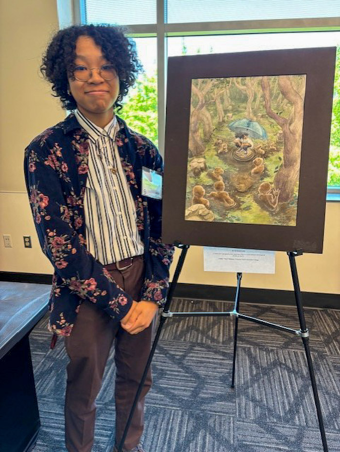 A person smiles and stands next to their poster display on an easel.