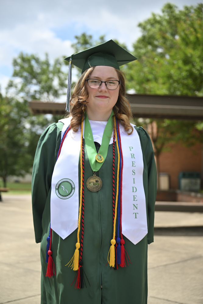 A person stands outside in a cap and gown.