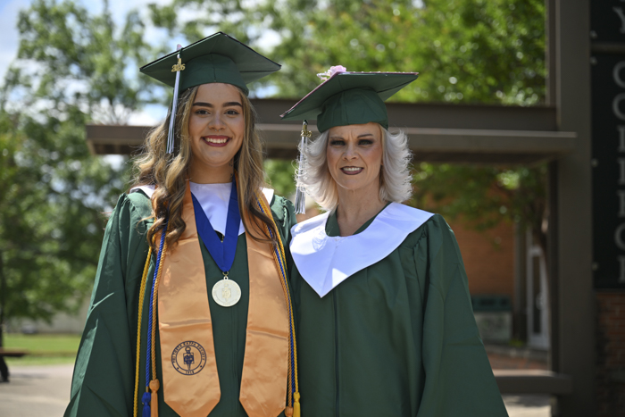 Two people stands outside in a cap and gown.
