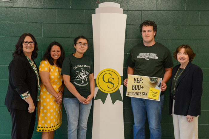 A group of people stand in front of a green wall. 