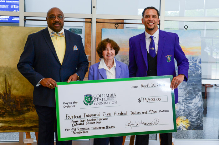 Three people are smiling and standing while holding an oversized check.