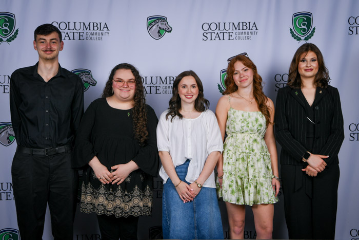 Five people stand in front of a background. 