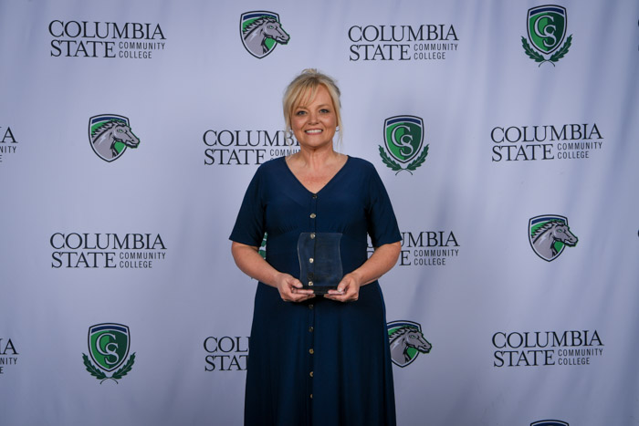 A person stands in front of a white background while holding a glass award.
