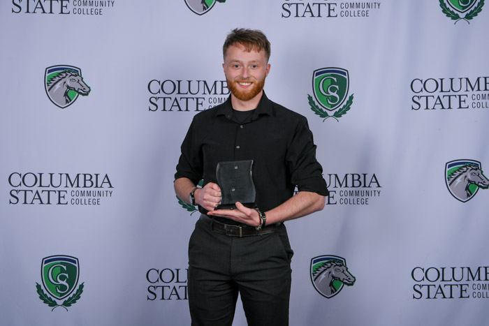 A person stands in front of a white background while holding a clear award.