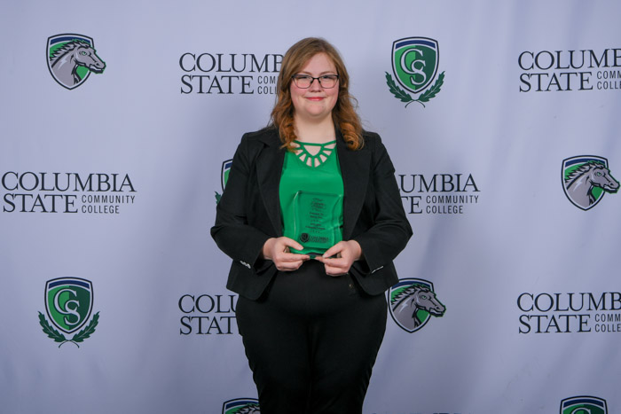 A person stand in front of a white background holding a clear award.