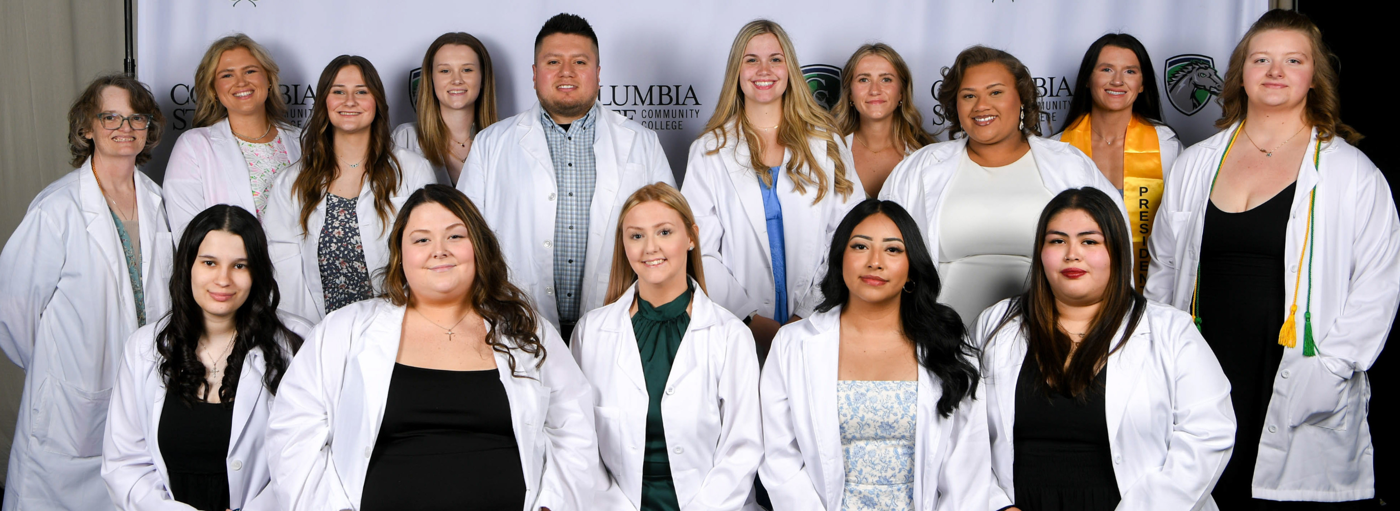A group of people stand in front of a white background.