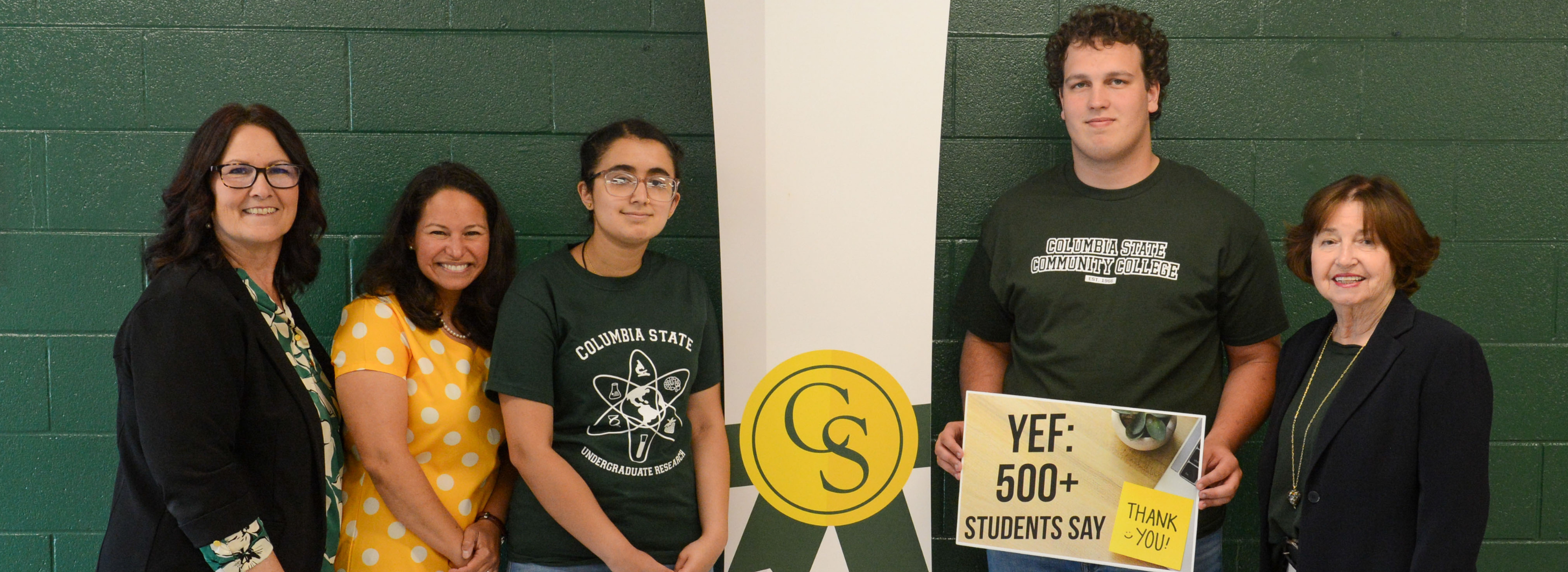 A group of people pose for a photo in front of a dark green wall.