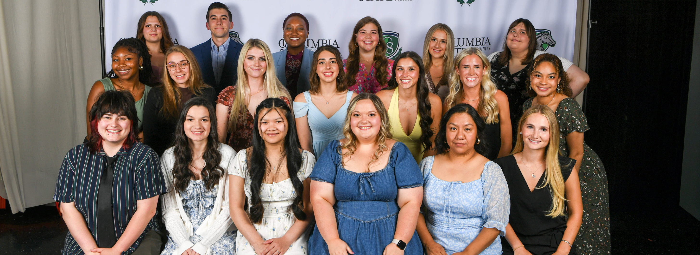 A group of people sit and stand in front of a white background.