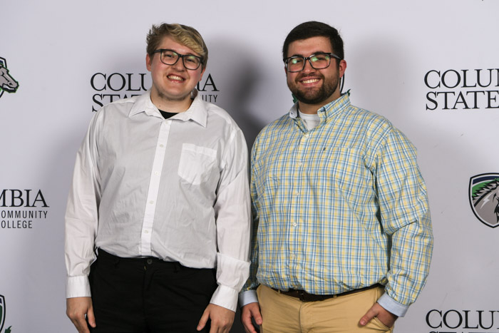 Two students wearing professional attire smile for a photo in front of a white background.