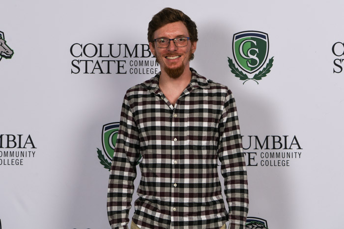 A student wearing professional attire smiles for a photo in front of a white background.