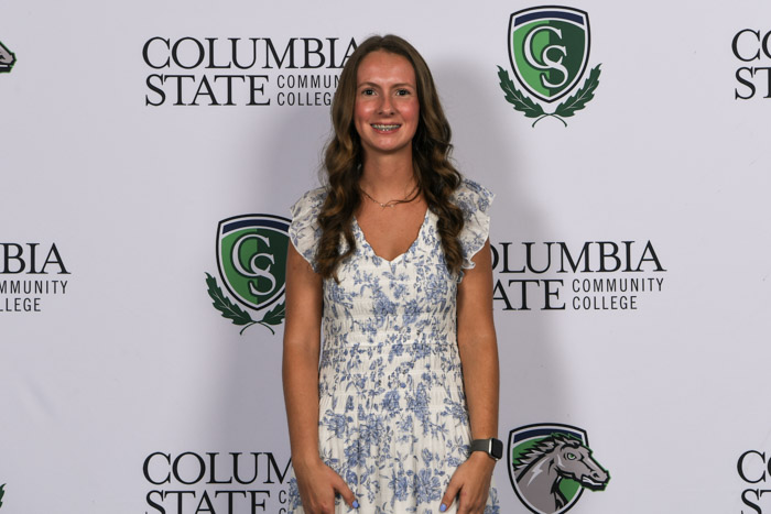 A student wearing professional attire smiles for a photo in front of a white background.