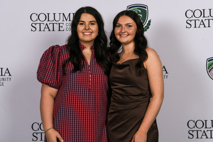 Two students wearing professional attire smile for a photo in front of a white background.