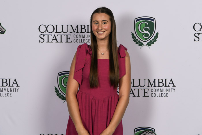 A student wearing professional attire smiles for a photo in front of a white background.