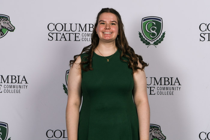 A student wearing professional attire smiles for a photo in front of a white background.