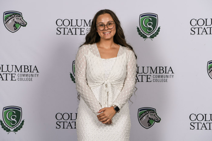 A student wearing professional attire smiles for a photo in front of a white background.