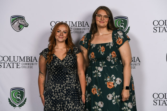 Two students wearing professional attire smile for a photo in front of a white background.