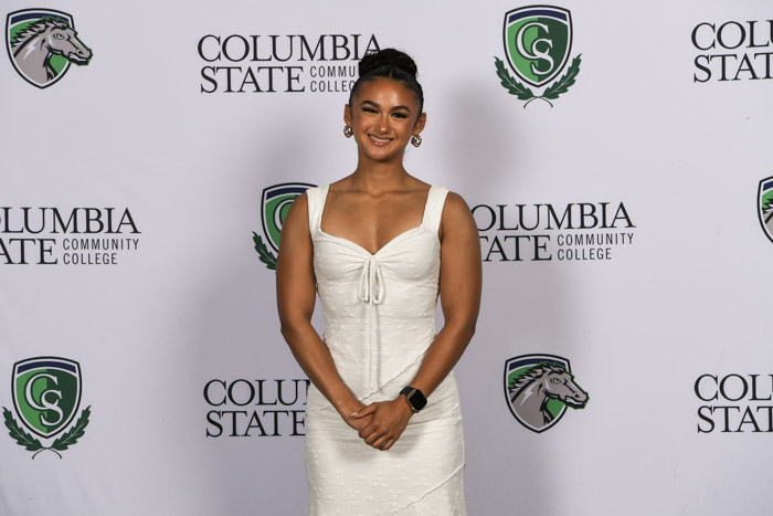 A student wearing professional attire smiles for a photo in front of a white background.