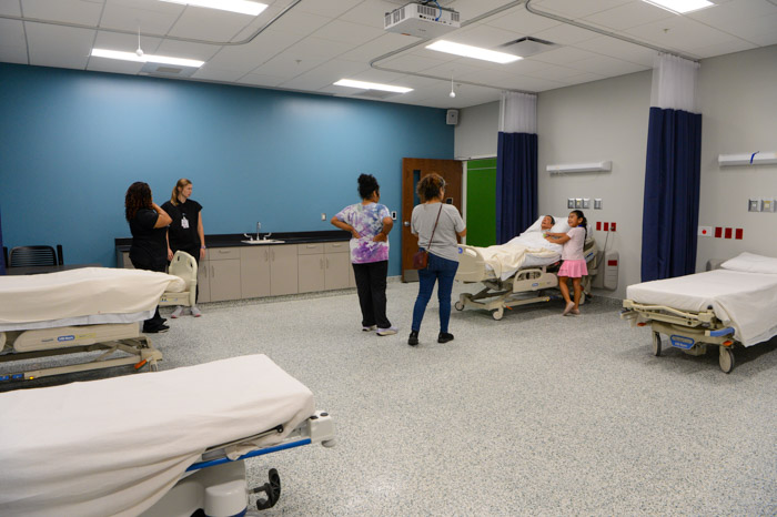 Four people and a child stand in a room that has four hospital beds.