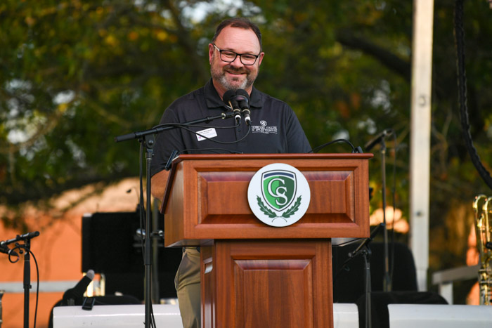 A person wearing a black collar shirt speaks at a wooden lectern.