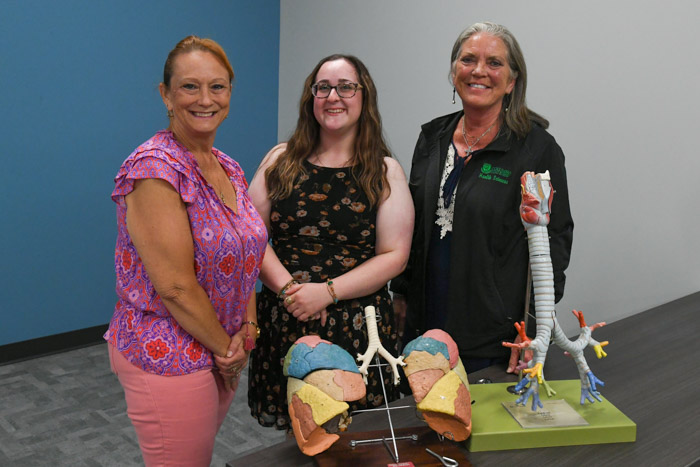 Three people stand smile for a picture in front of two anatomical displays of two lungs and bronchioles.