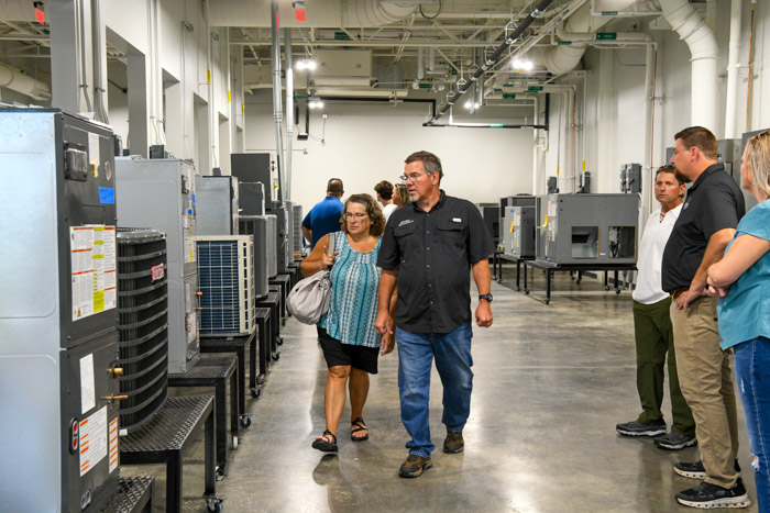 People walk through a room with several air conditioning and heating units. 