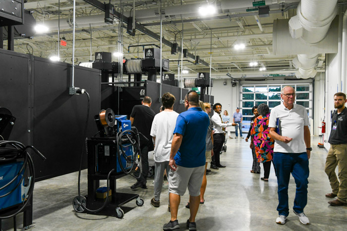 People walk through an indoor labe with welding machines and equipment.