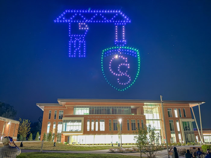 Flying drones create an image of a crane pulling up the Columbia State shield logo in the night sky above the Southern Regional Technology Center.
