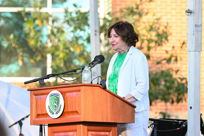 A person wearing white and green speaks at a wooden podium.
