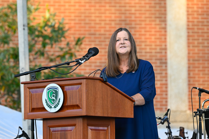 A person in a blue dress stands at a wooden podium while speaking.