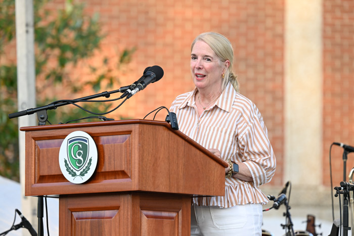 A person in a tan and white striped shirt speaks behind a wooden podium.