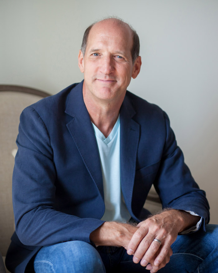 A person sits wearing a blue suit jacket and blue jeans.