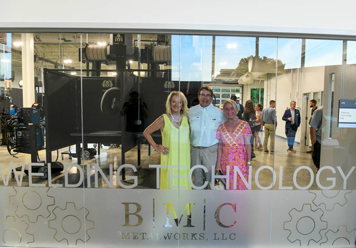 Three people stand behind a wall of glass smiling for a photo.