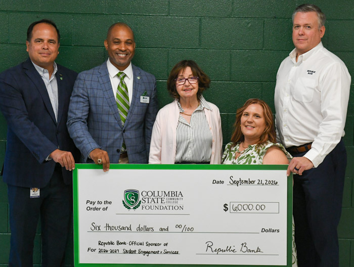 Five people hold a large signed check while posing for a photo.
