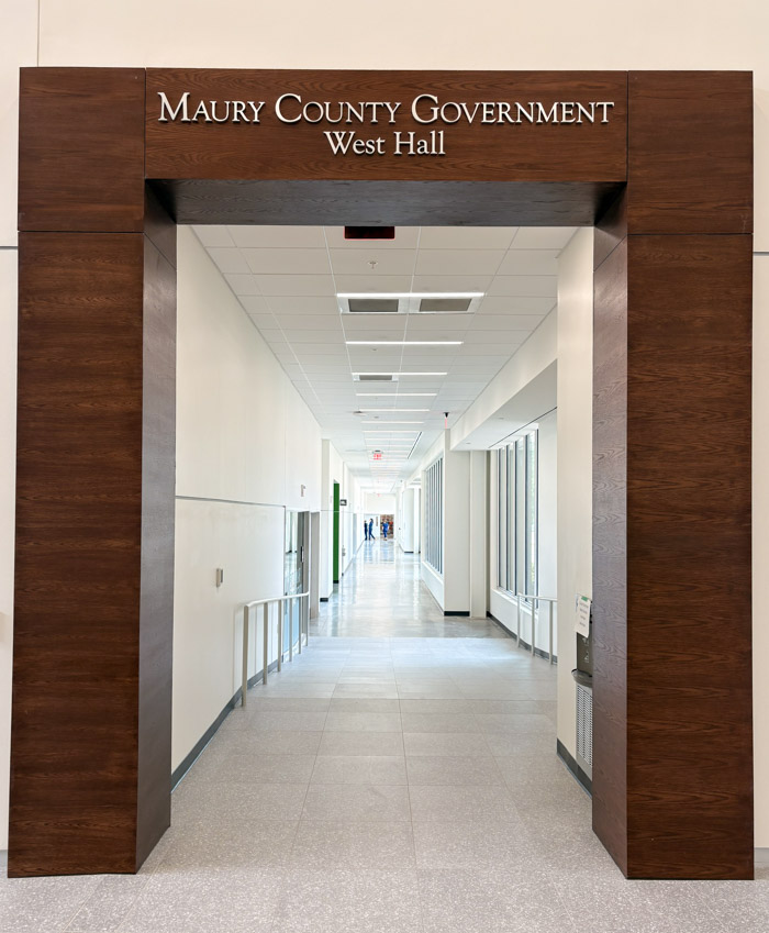 An entranceway to a hallway has tet above it that says, "Maury County Government West Hall."