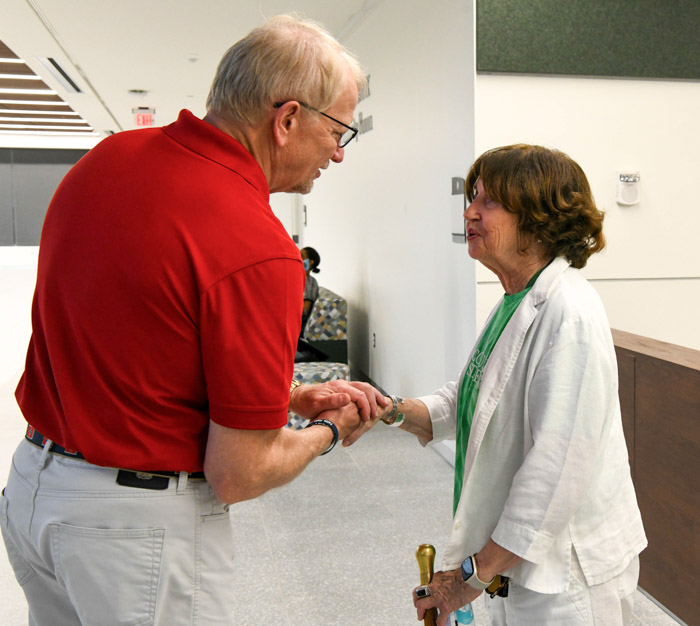 A person in a red shirt shakes the hand of a person wearing a white and green shirt.